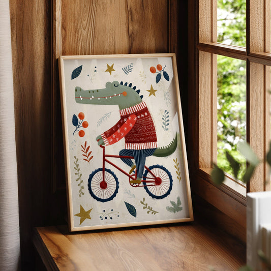 A vertical art print featuring a green crocodile riding a red bicycle. The crocodile is wearing a red and white patterned sweater and blue striped pants. The background is cream with stylized leaves, berries, and gold stars scattered around.
