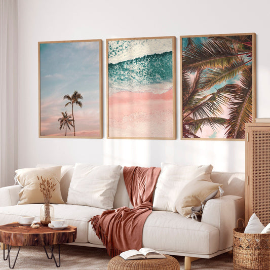 Beach wall art set of 3 prints featuring palm trees, aerial pink sand beach with turquoise waves, and tropical palm fronds.