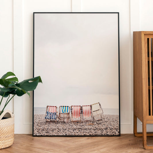 Colorful striped beach chairs on a pebble beach facing the ocean, coastal wall art print.